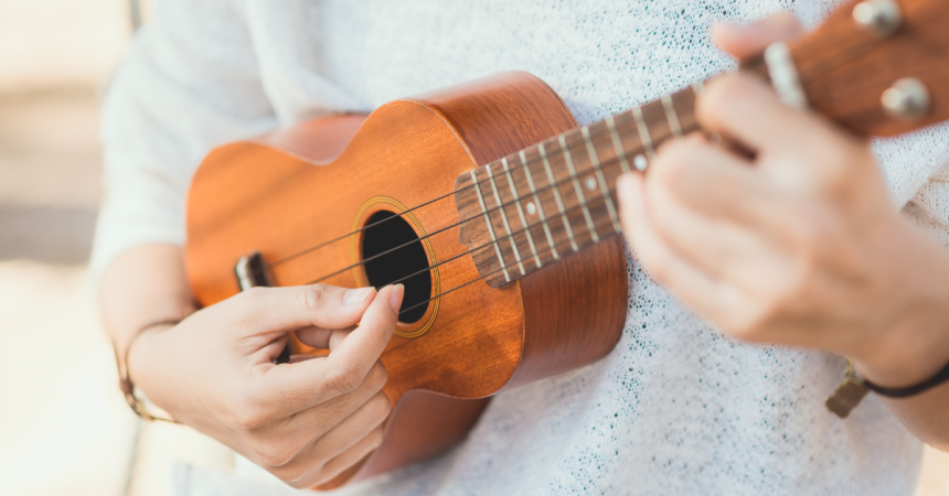 a pair of hands playing a ukulele, a small, guitar-like musical instrument.