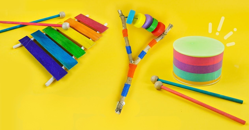 Three homemade percussion instruments: a xylophone, a drum with sticks and a rattle made from a forked branch and bottle caps on a string.