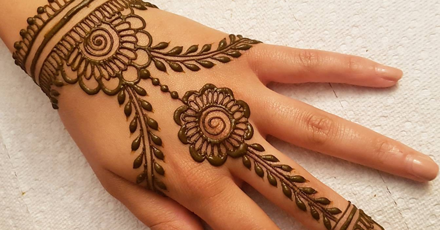A photo of the back of a hand, with swirling dark brown patterns shaped like flowers and other geometric designs.