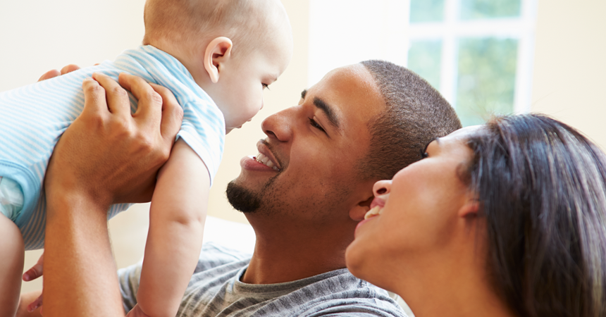 A Black man and woman cuddle and coo at a light-skinned infant.