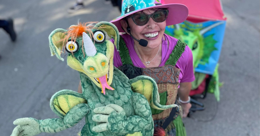 Vikki Green smiles and poses with a large green dragon puppet.