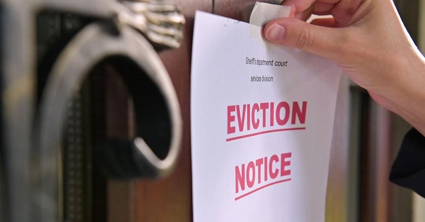 A hand tapes a sheet of paper with "EVICTION NOTICE" on it in large red letters on the front door of a home.