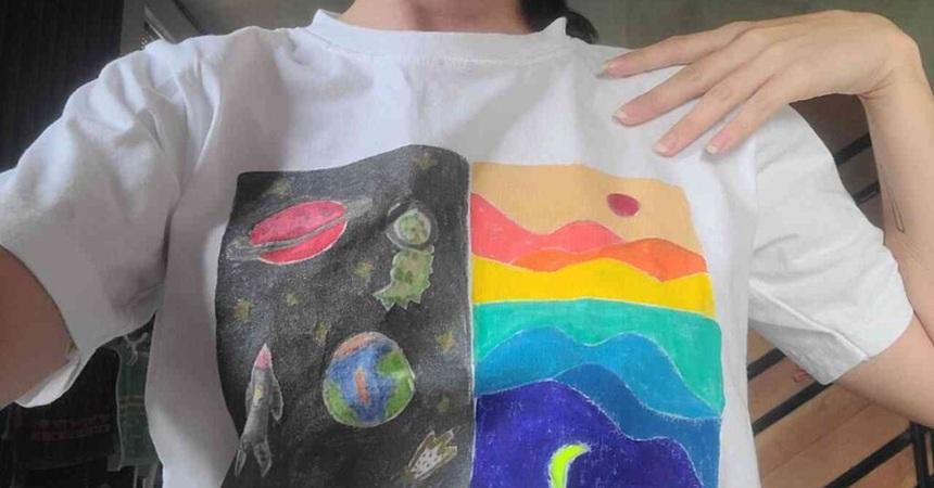 A person wearing a white t-shirt with space and landscape images drawn on with fabric pastels.