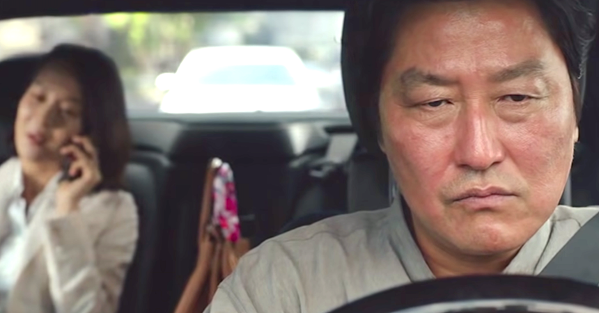 In a scene from Parasite, Ki-Taek (played by Song Kang-ho) frowns in annoyance while driving Yeon Kyo (played by Cho Yeo-jeong), who is having a cell phone call in the back seat.