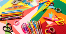 An assortment of colored pencils, gel pens, and scissors scattered over sheets of multicolored construction paper.