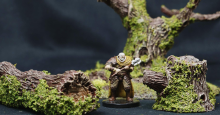 A miniature of a human fighter in heavy armor is surrounded by plastic trees covered in lichen.