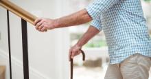 A man uses a cane and handrail to climb a set of stairs.