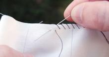 A pair of hands sews two pieces of plain muslin together.