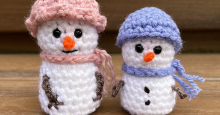 Two small plush snowmen made of yarn, wearing hats and scarves.