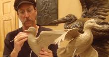 Sculptor Stefan Savides uses a carving tool to shape a life-sized clay statue of a duck in flight.