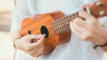 a pair of hands playing a ukulele, a small, guitar-like musical instrument.