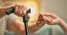 An elderly person holds a cane in one hand and another person's hand in the other.