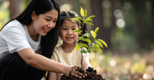 A mom and her child press a tree sapling into freshly-dug soil.
