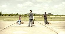 On the poster for Meeting with Pol Pot, the three leads stand on an empty tarmac with their luggage.